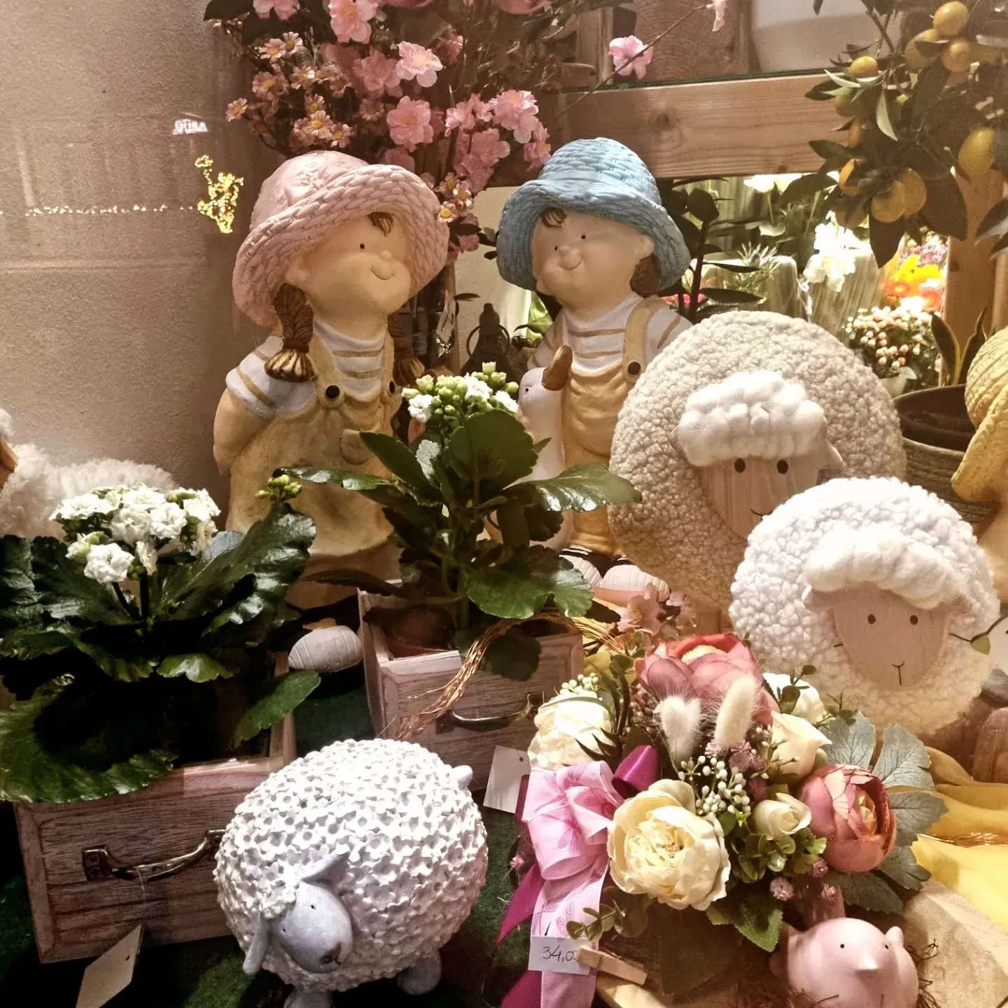Figurine fantasiose tra fiori e verde in un giardino dai toni tenui e pastello.