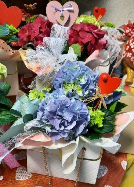 Due coloratissimi cestini regalo floreali con nastri e decorazioni a forma di cuore su un tavolo di legno.