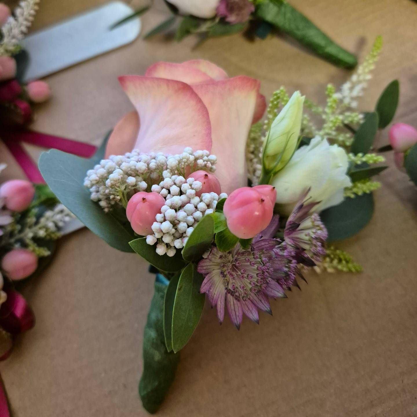 Bouquet da sposa dai toni pastello con rosa rosa, boccioli bianchi e fiori viola su un tavolo di legno.