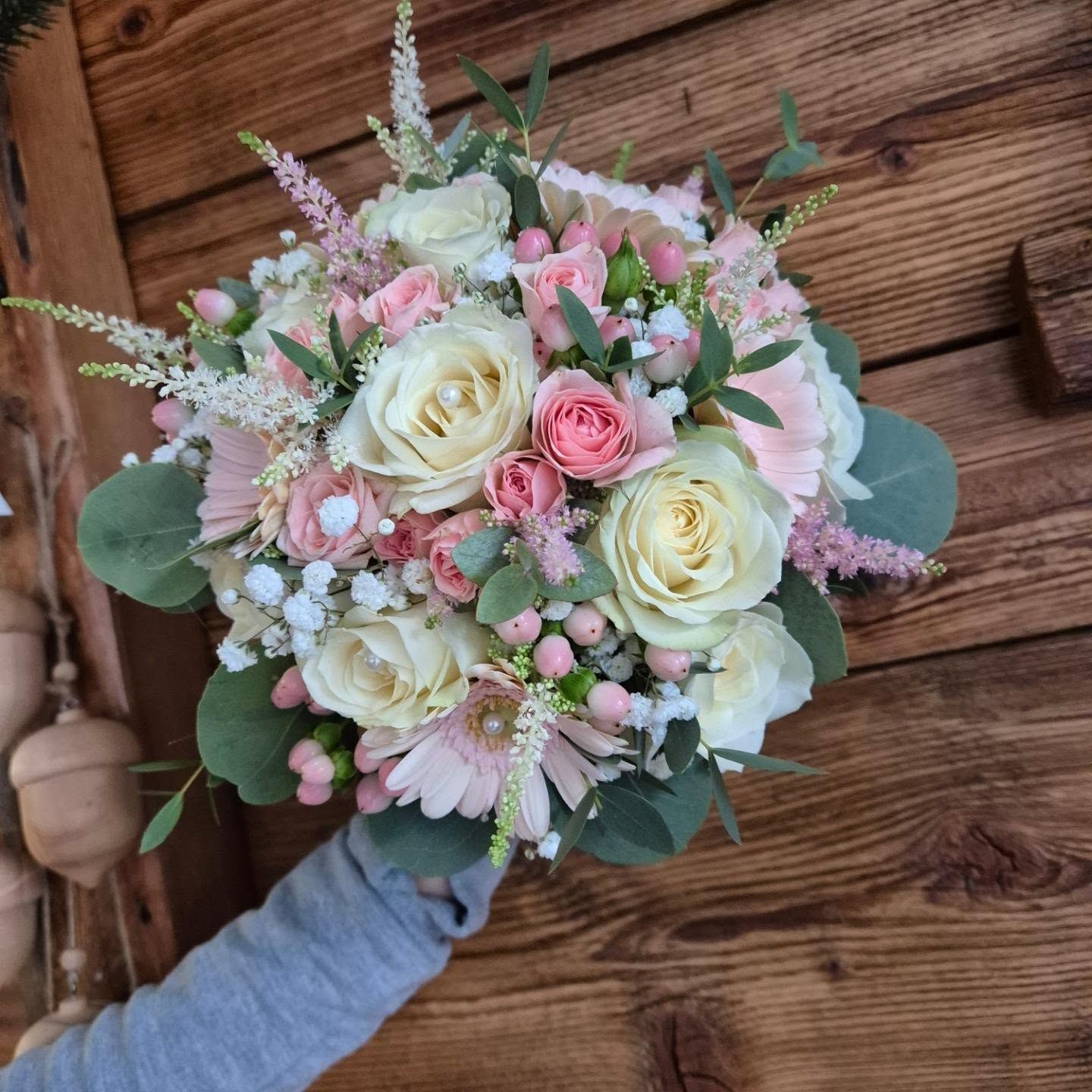 Bouquet di rose bianche e rosa con verde, tenuto a mano su una superficie di legno.