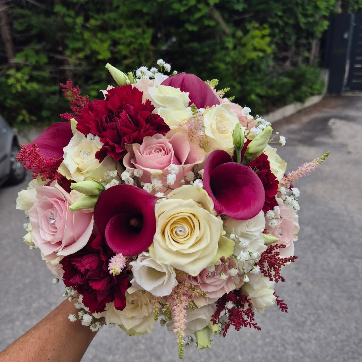 Bouquet di fiori rosa, crema e rosso intenso con rose e calle, da tenere in mano all'aperto.