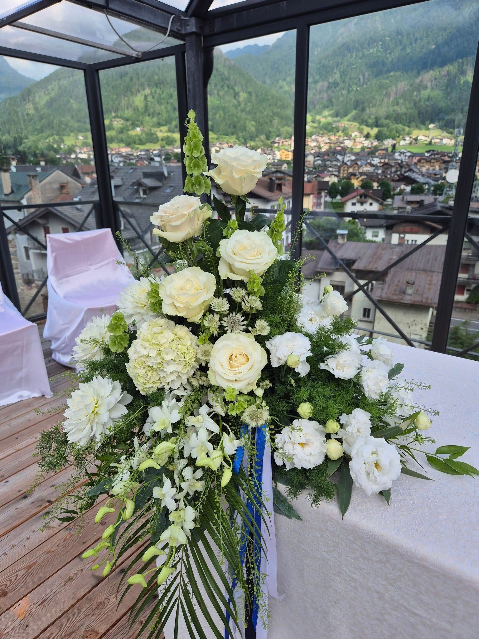Composizione floreale di rose bianche su un tavolo da terrazza con vista su un villaggio e sulle montagne.