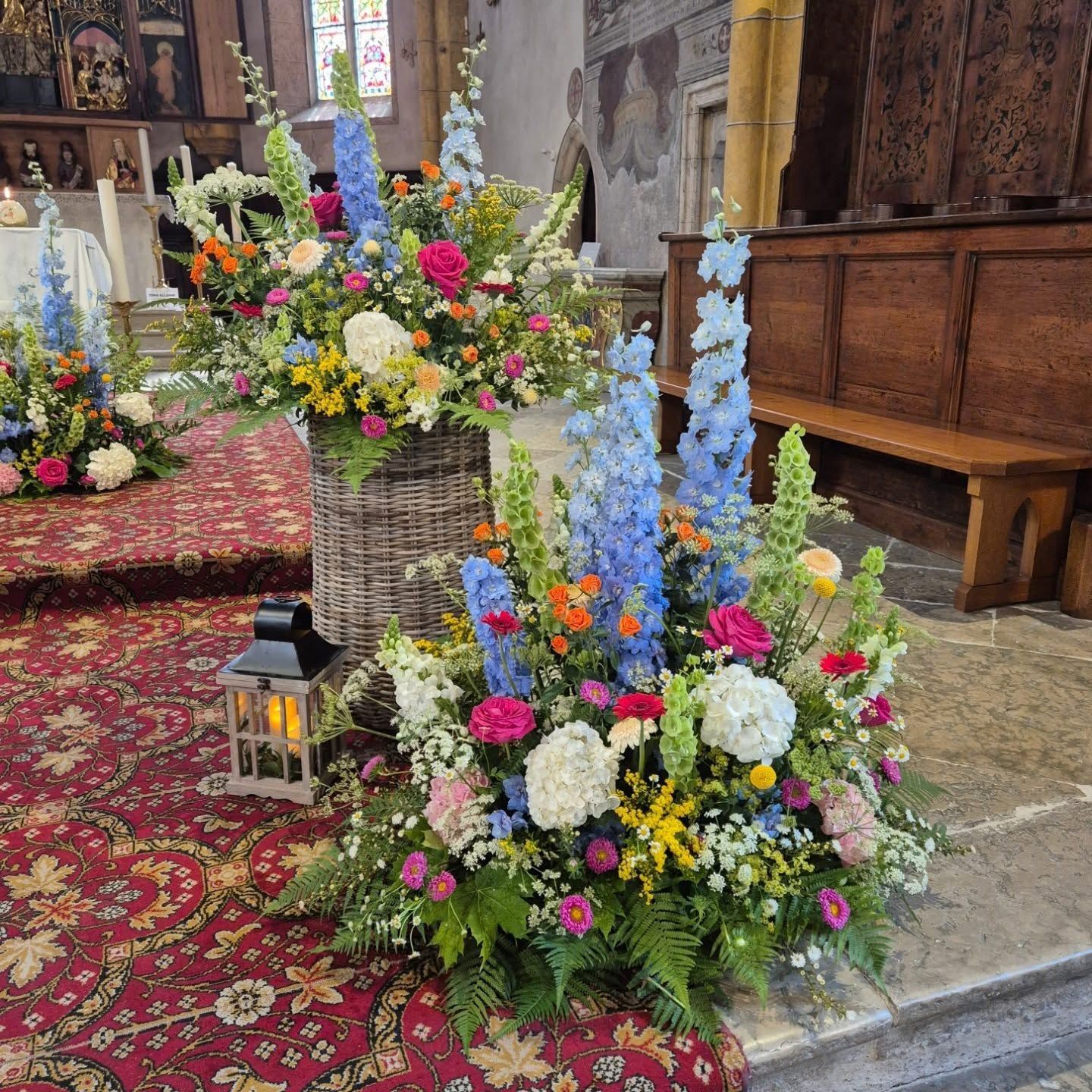 Composizioni floreali con fiori blu, rosa, bianchi e gialli all'interno di una chiesa, su un tappeto decorato.