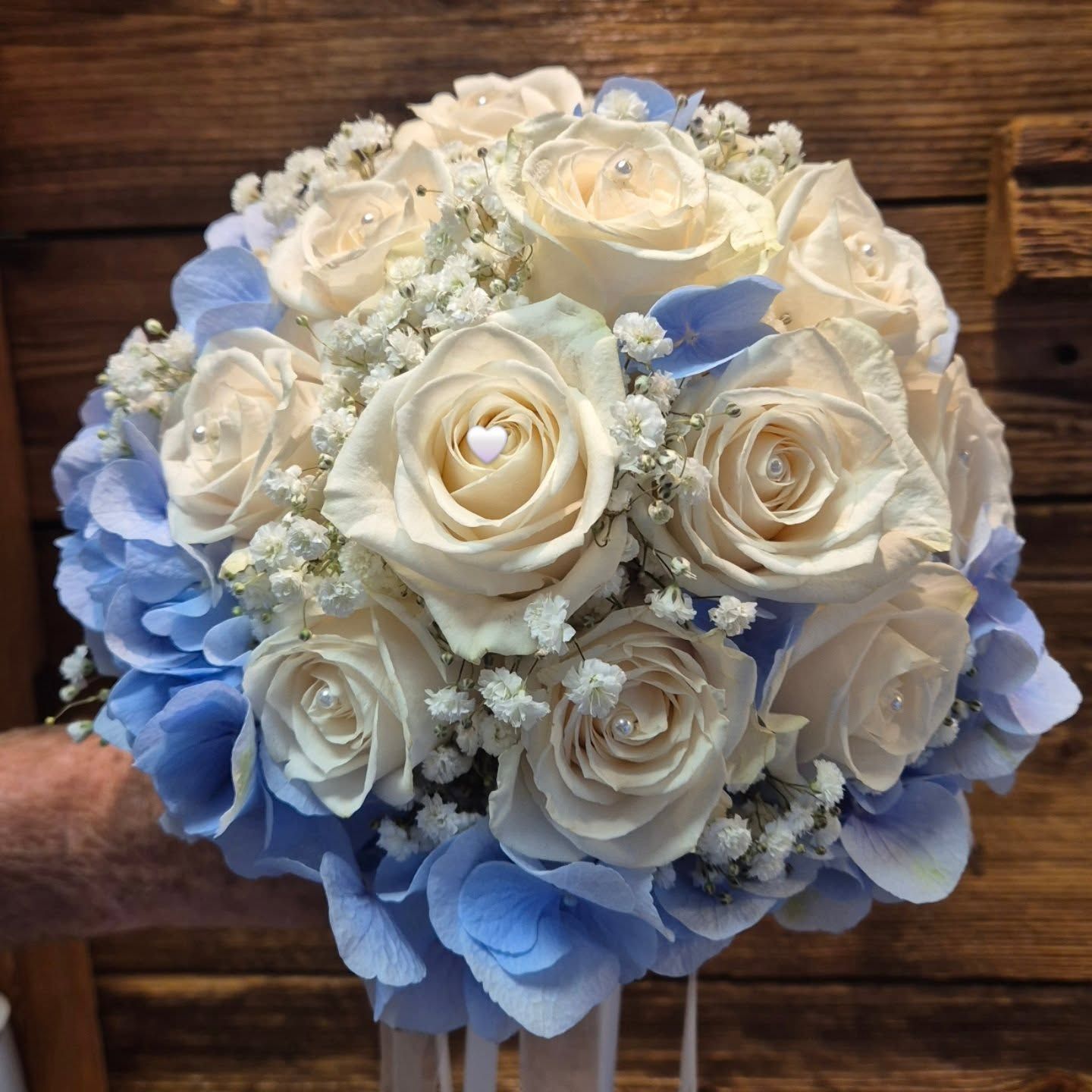Bouquet di rose bianche e azzurre, tenuto in mano, con sfondo di legno.