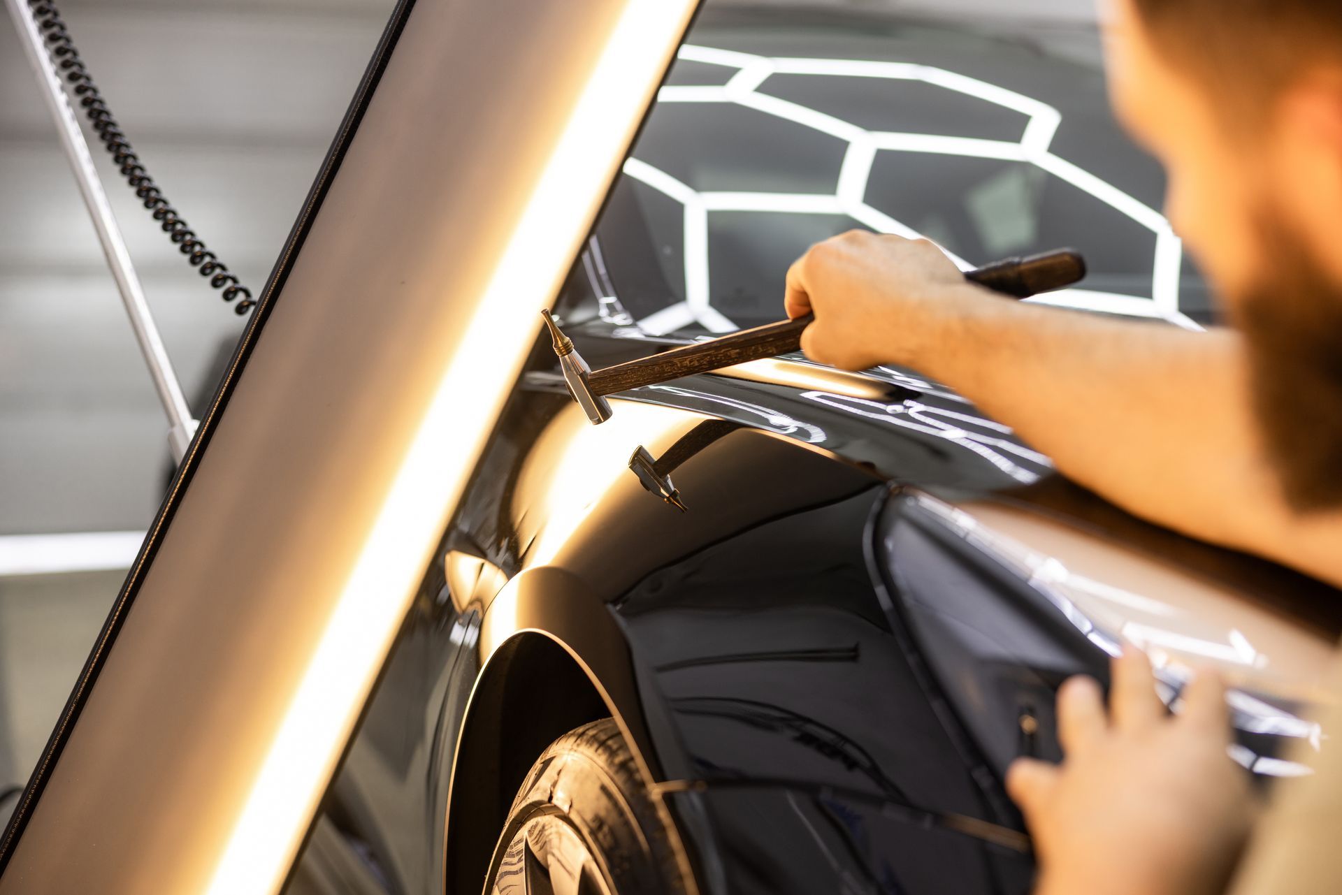 Specialist repairing hail damage on car panel in garage.
