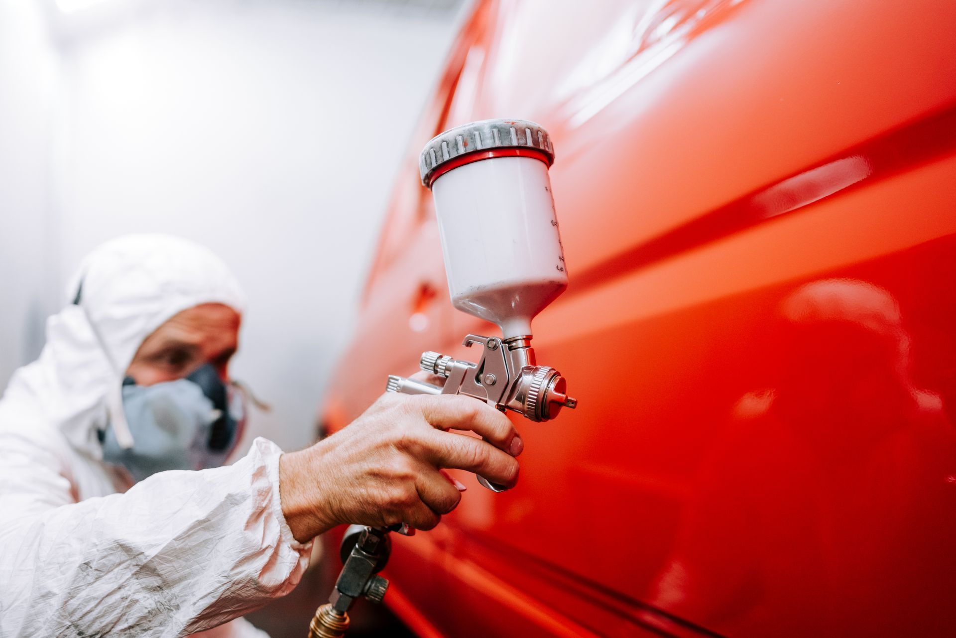 A car spray painter painting a car red in a painting box, wearing protective gear. A car spray painter painting a car red in a painting box, wearing protective gear.