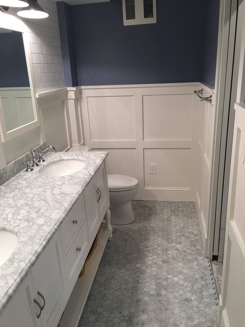 Bathroom with a white vanity and wainscoting, blue walls, patterned tile flooring, and a white toilet.