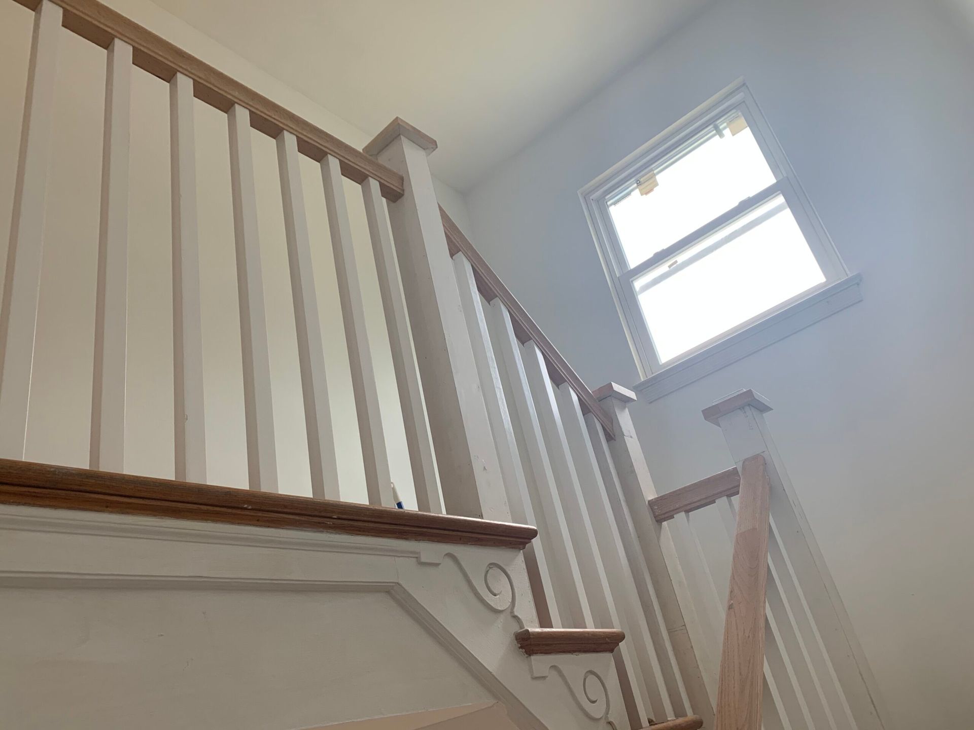 Wooden staircase with white spindles and brown handrails, leading toward a window.