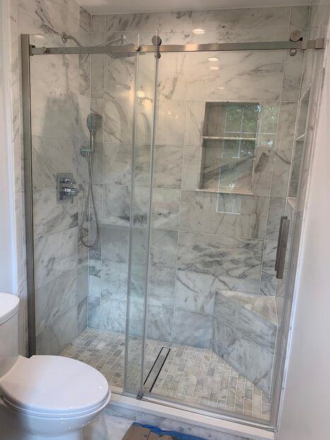 Marble-tiled shower with glass sliding doors, chrome fixtures. Includes a built-in shelf. Toilet visible in the foreground.