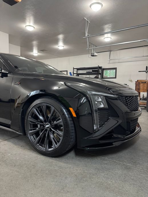 Black Cadillac SUV parked in a garage, front-left view under bright ceiling lights.
