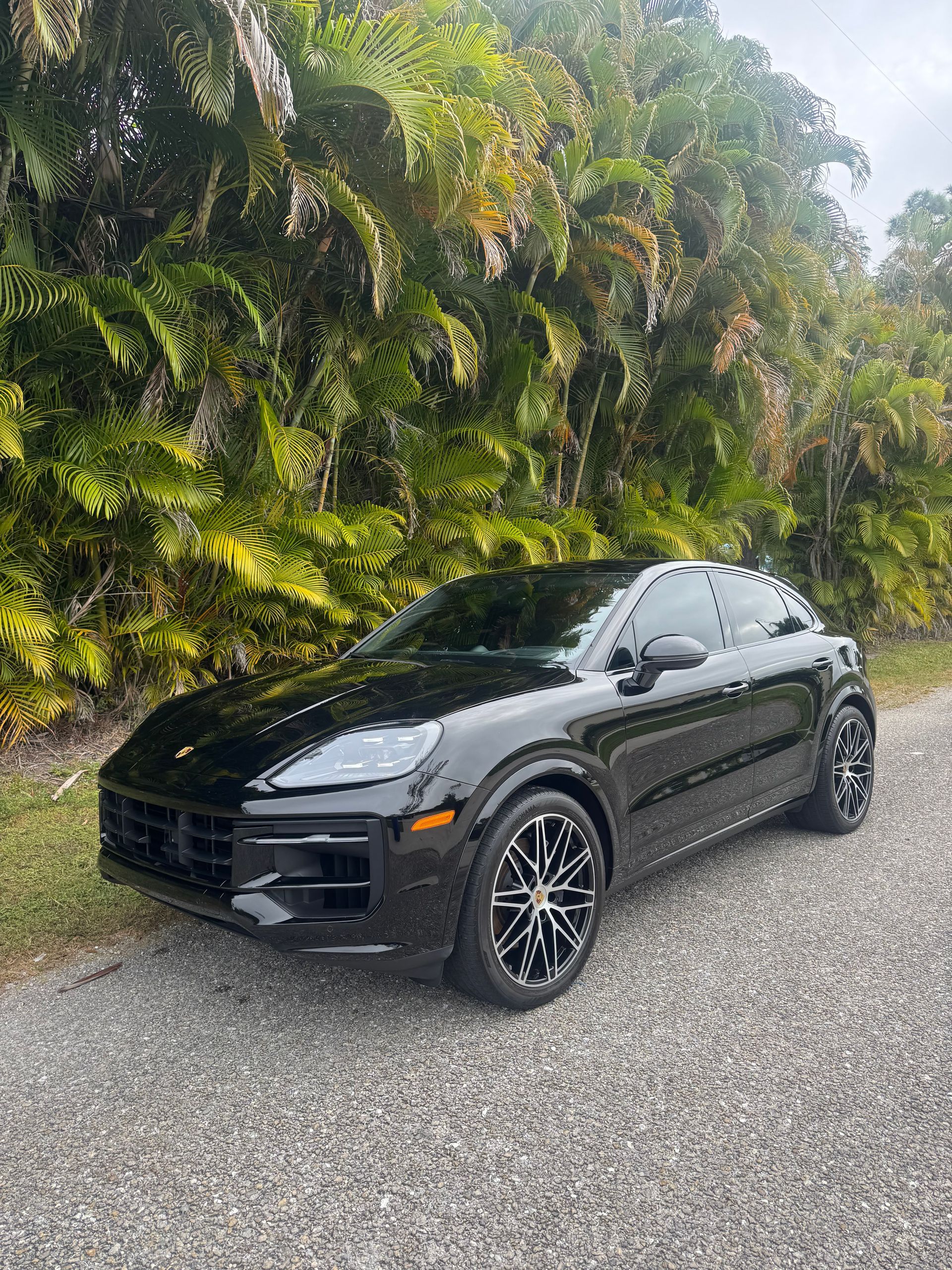 Black SUV parked on gravel beside a lush green hillside.