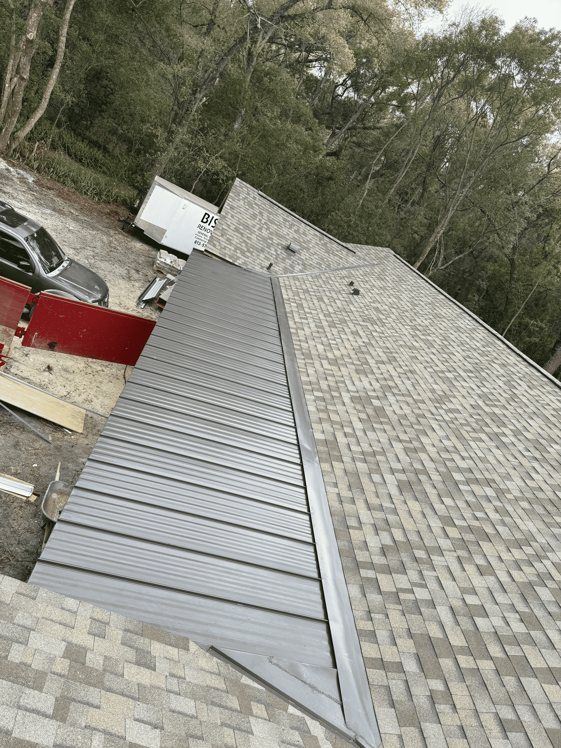 Gray metal roof section being installed next to existing asphalt shingles.