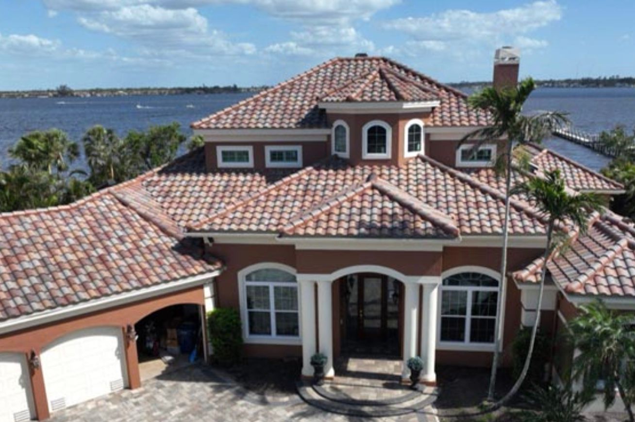 A house with a dark gray shingle roof and a tan exterior. Other houses are in the background.