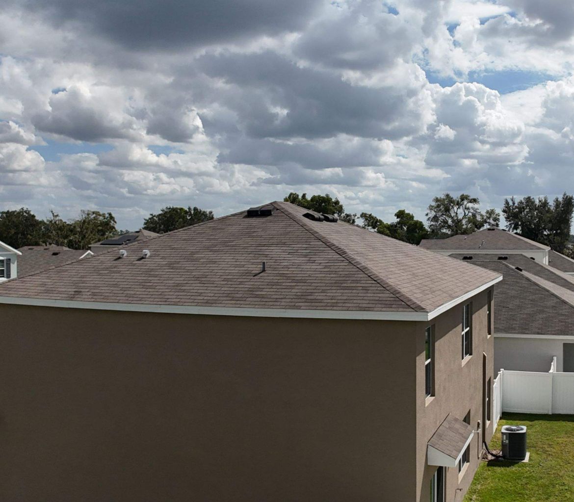 Brown house with a gray shingled roof under a cloudy sky.