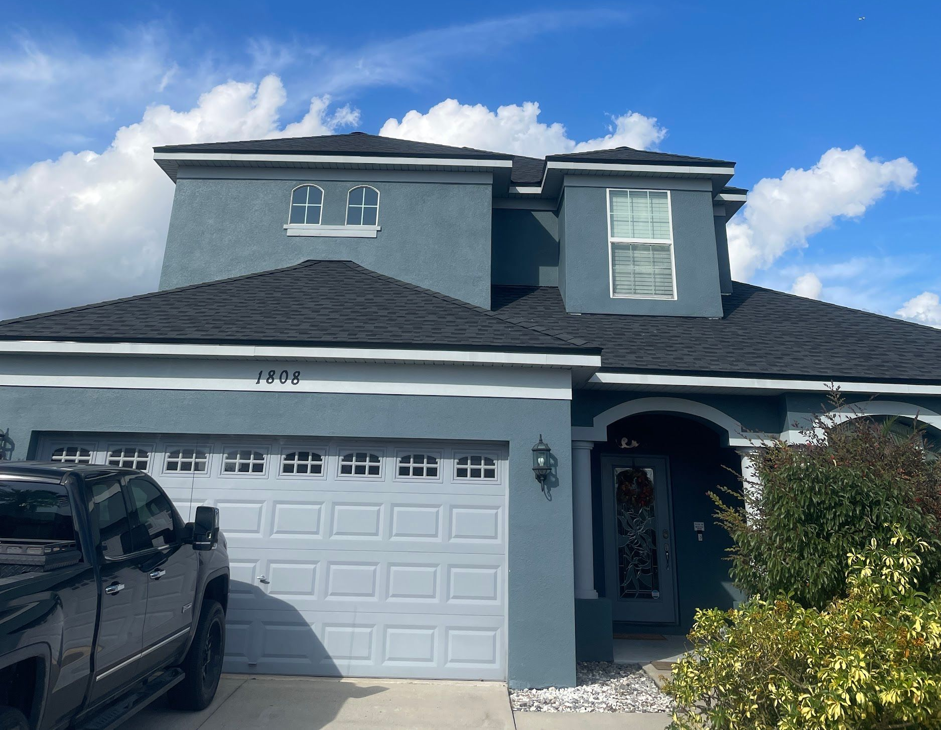 Blue two-story house with a gray garage door and a dark roof. A black truck is parked in the driveway.