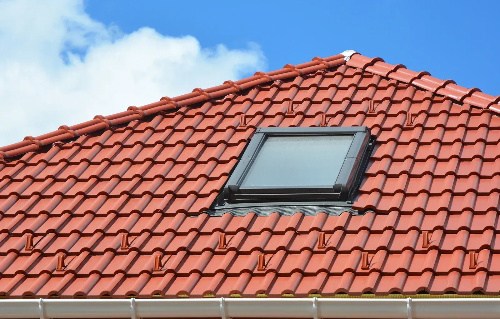 Red tiled roof with a skylight, set against a blue sky with white clouds.