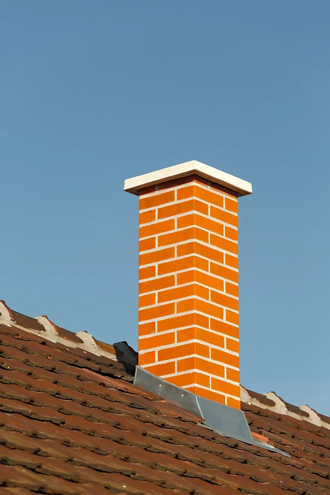 Brick chimney on a tiled roof against a clear blue sky.