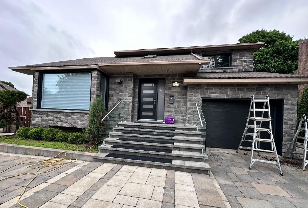 Une grande maison en briques avec une porte de garage noire est en train d'être peinte.