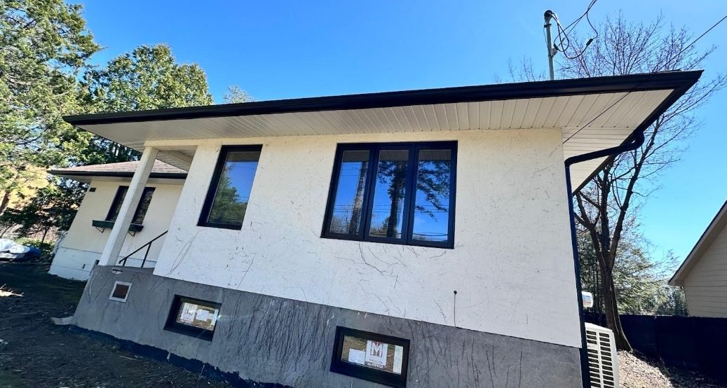 Une maison blanche avec des fenêtres noires et un ciel bleu en arrière-plan.