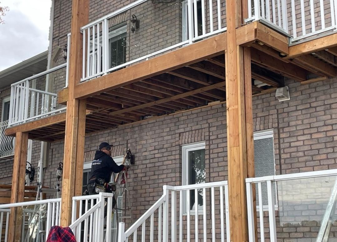 Un homme se tient sur le balcon d'une maison en briques.