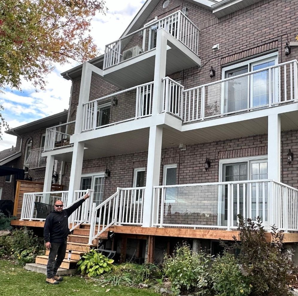 Un homme se tient devant une grande maison en briques avec des balcons.