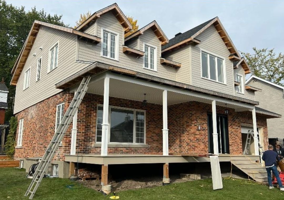 Une grande maison en briques avec un porche et une échelle devant.