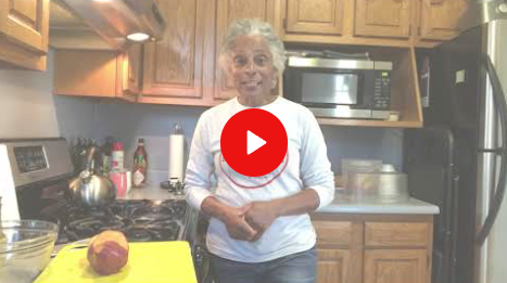 Woman standing in a kitchen beside a yellow cutting board with an onion and a red play button overlay