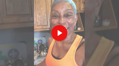 Woman in orange tank top smiling in a kitchen, with a red play button overlay.