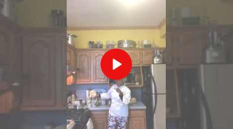 Person standing in a kitchen beneath a red play button overlay.