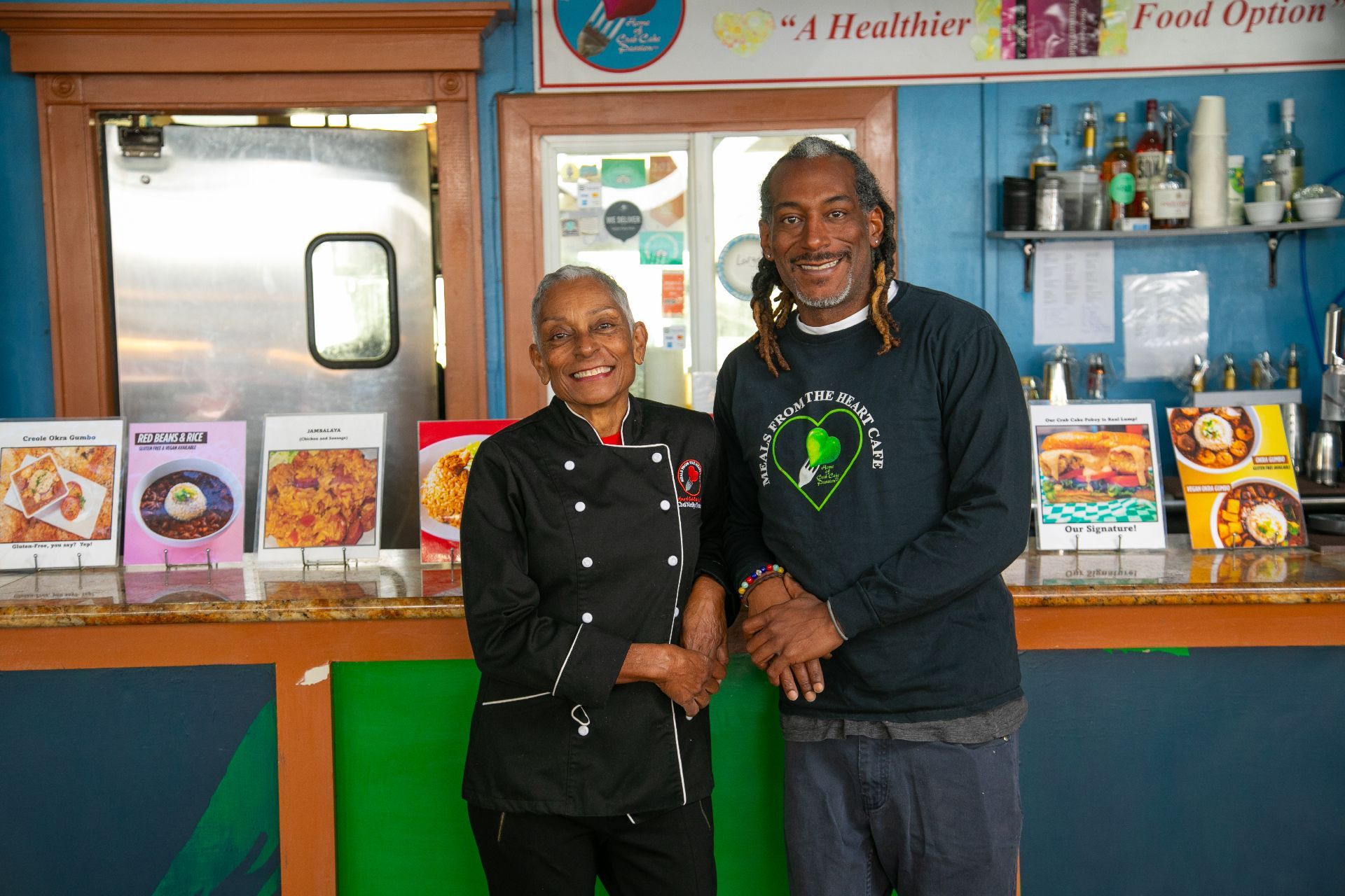 Two people smiling behind a health food counter with colorful cereal boxes and shelves of products