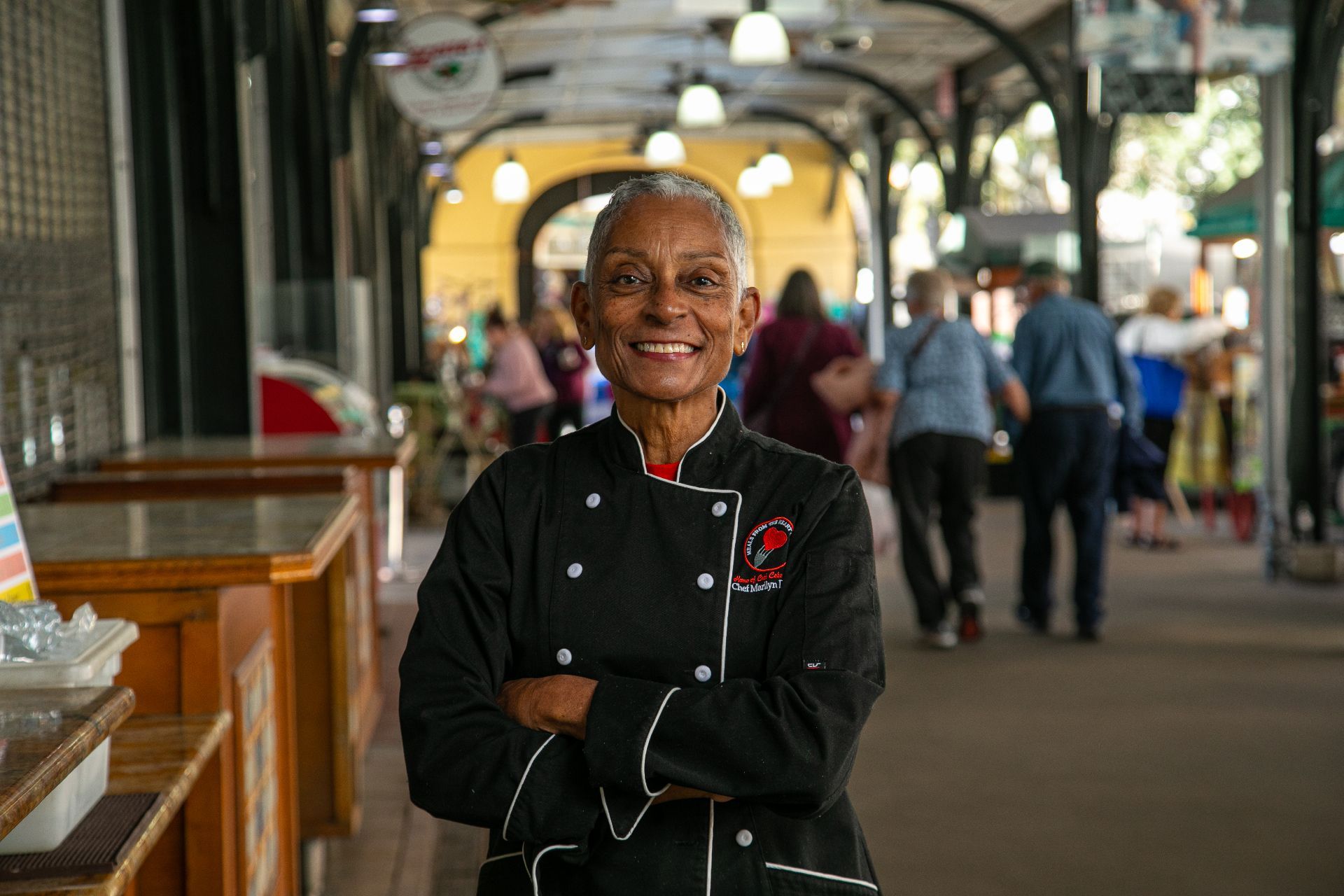 Smiling chef in black uniform standing in a covered outdoor market corridor