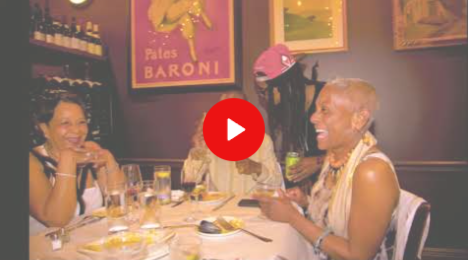 Two people chatting over dinner in a cozy restaurant, with wine glasses and candles on the table.