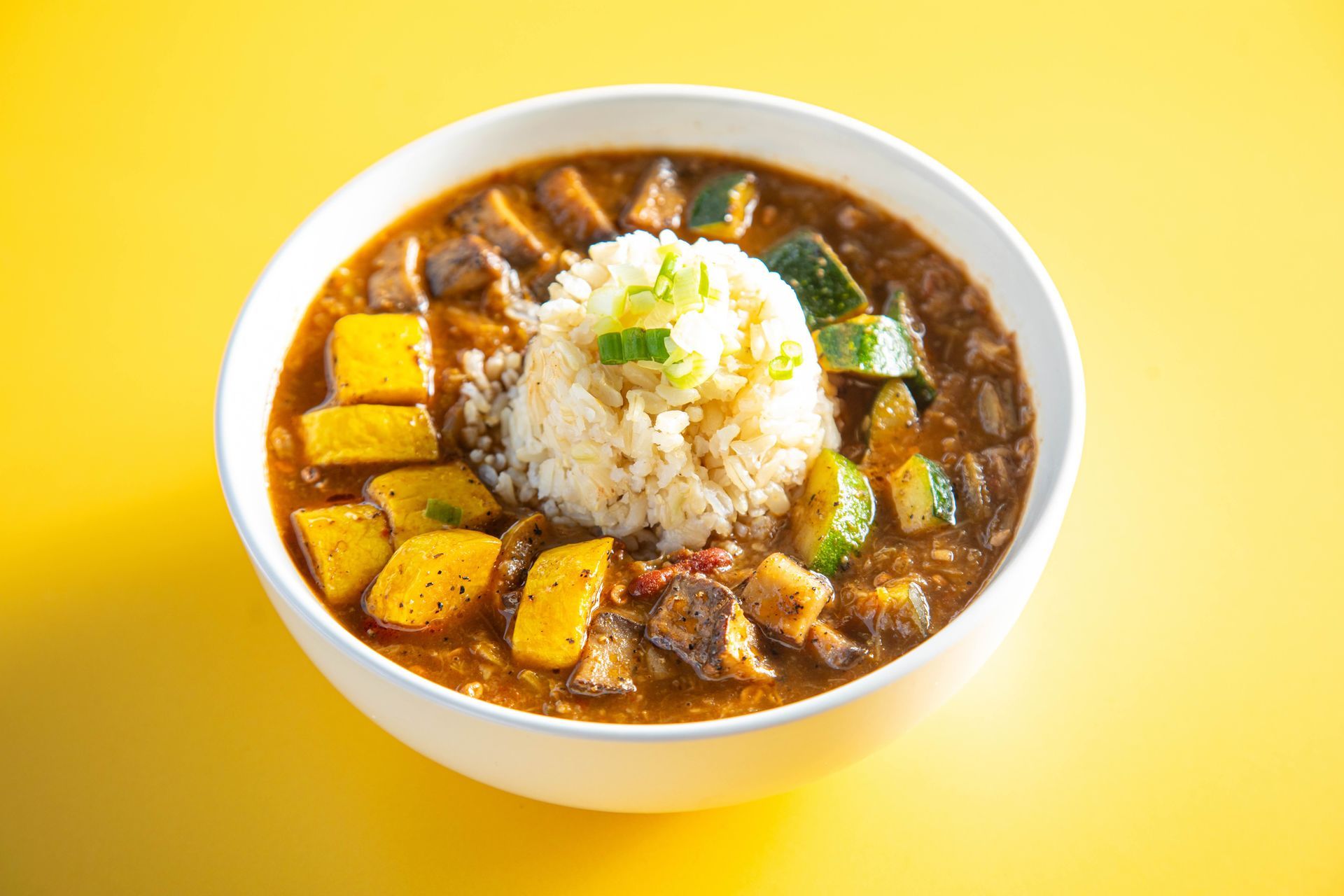 Bowl of curry with rice, yellow vegetables, and herbs on a bright yellow background