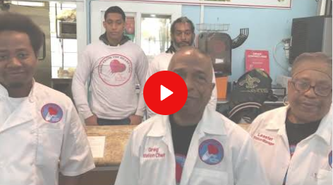 Four men in white lab coats stand in a workshop, with one man in front and a red play button overlay.