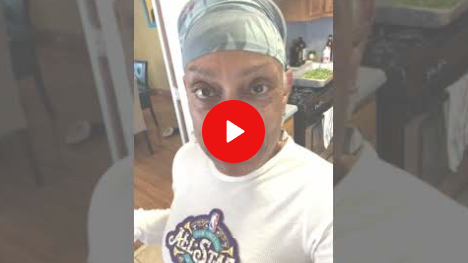 Woman in a white shirt and headscarf taking a selfie indoors, with a red play button overlay.