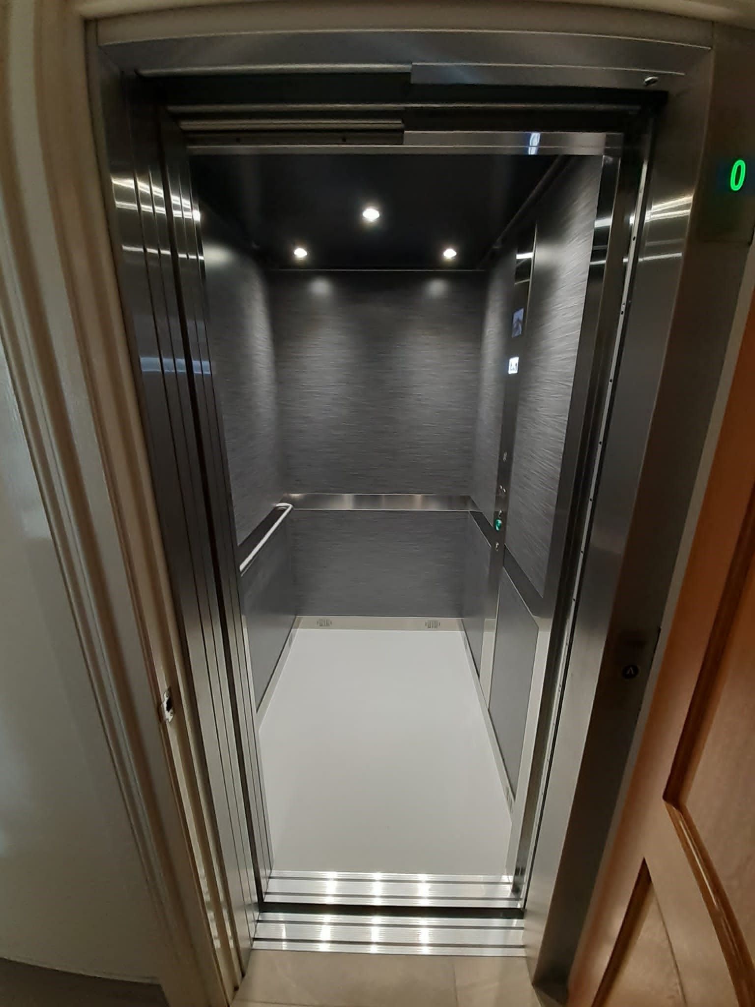 Interior of a modern home elevator with stainless steel accents, gray walls, and a white floor.
