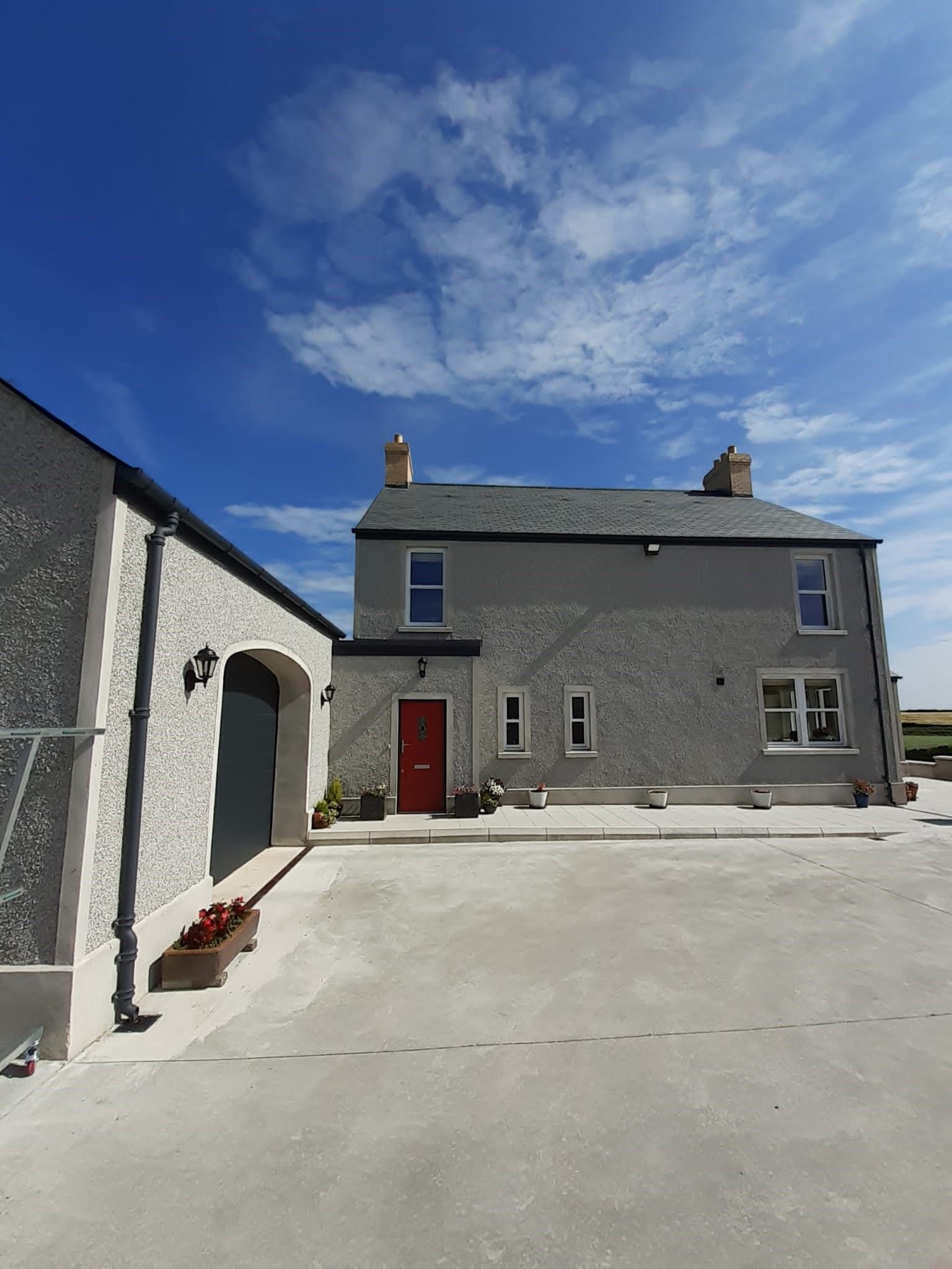 Gray house with attached garage and patio, set on a large concrete driveway under a blue sky.