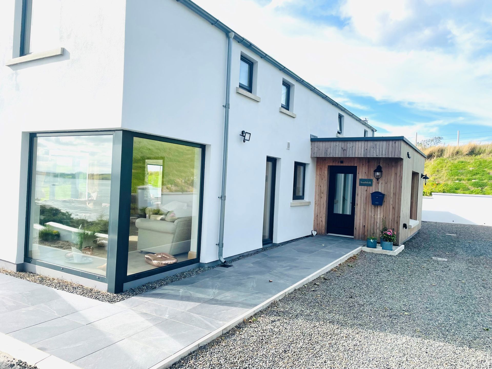 White modern house with glass corner, door under wooden canopy, and gravel walkway.