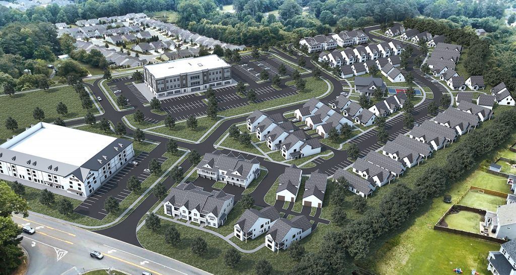 Aerial view of a suburban housing development with rows of houses, roads, trees, and apartment buildings.