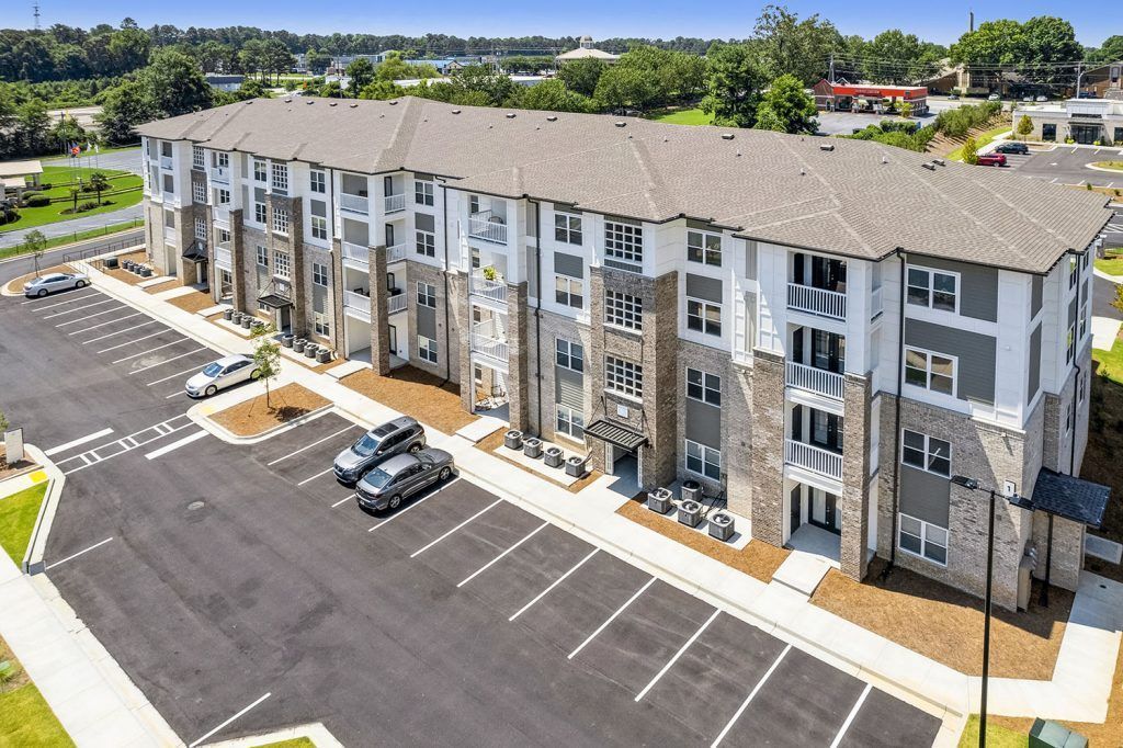 Aerial view of a modern apartment complex with a parking lot and surrounding trees