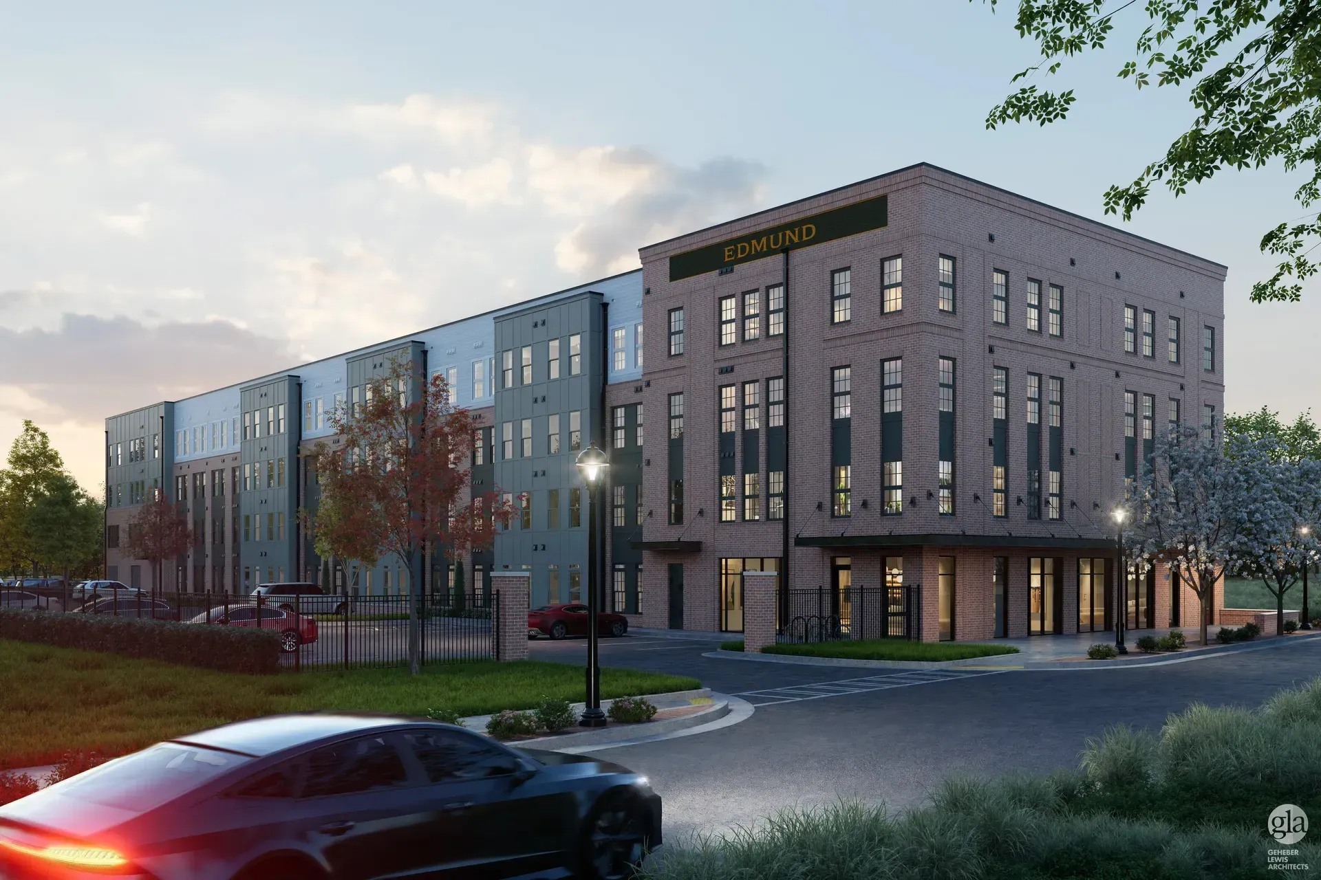 Modern brick apartment building at dusk with lit windows, streetlights, and cars in front