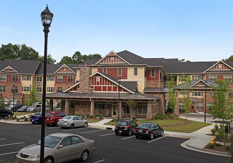 Parking lot in front of a multi-story building with red and tan siding, a brown roof, and a stone facade.