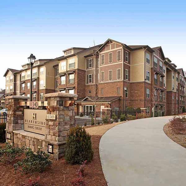 Apartment building entrance with stone sign, brick balconies, and curved walkway under a blue sky