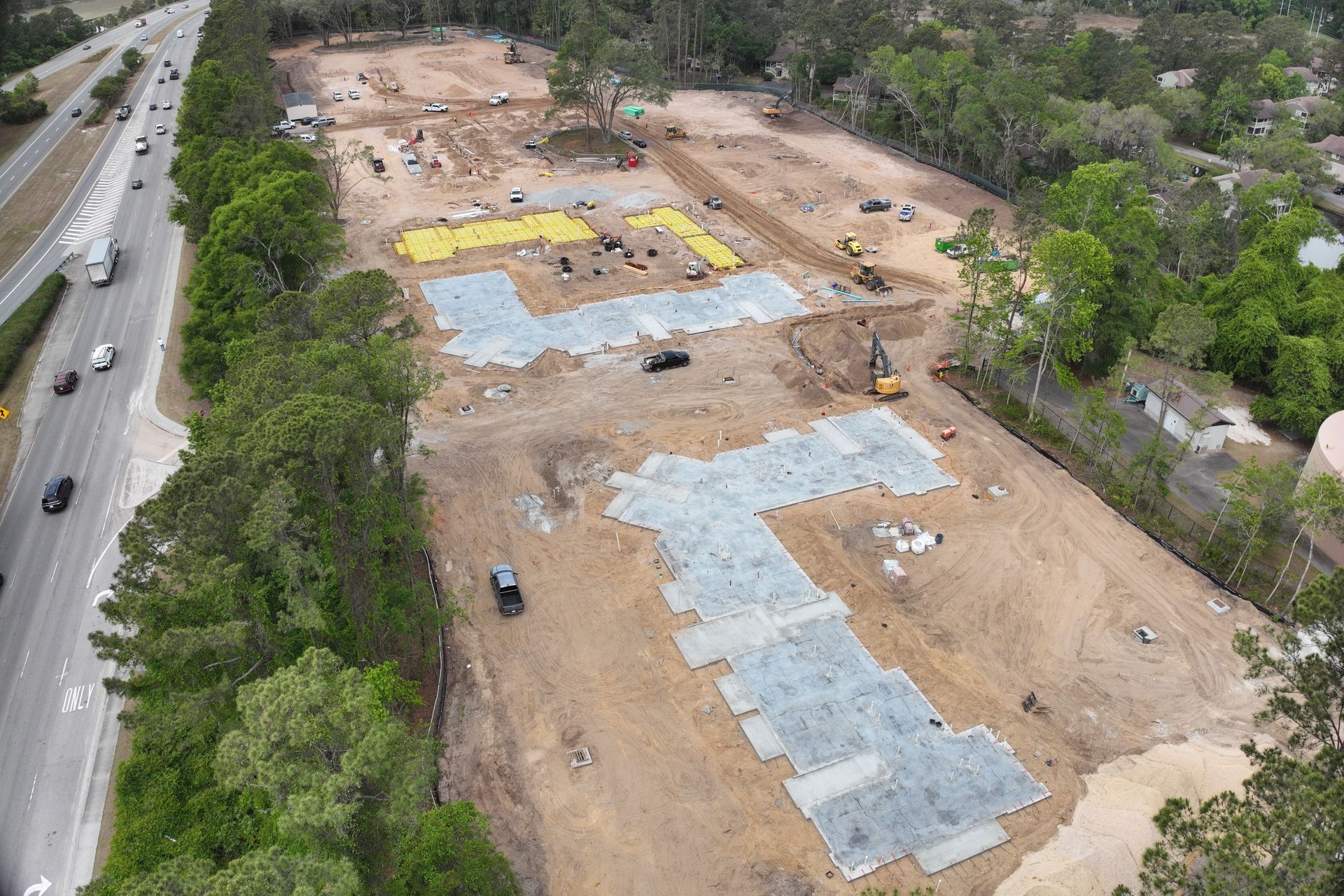Aerial view of a large construction site beside a road, with excavators and dirt-covered groundwork.