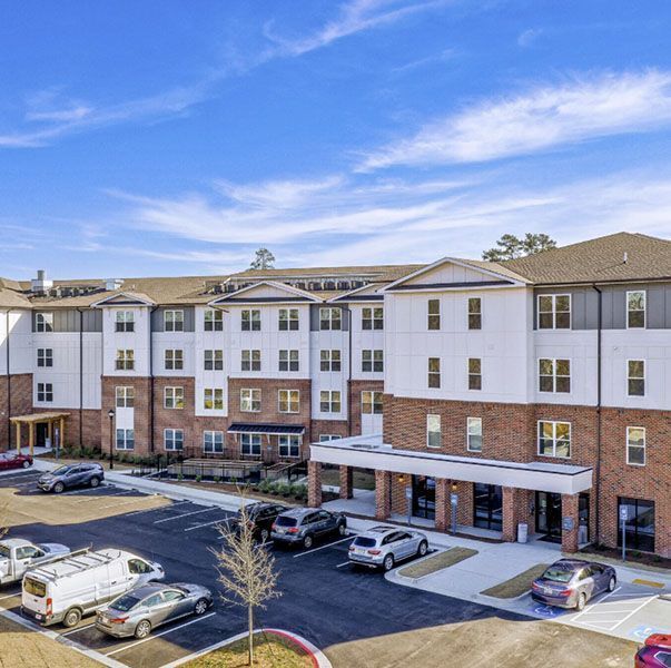 Multi-story apartment building with brick and white siding, parked cars, and a clear blue sky