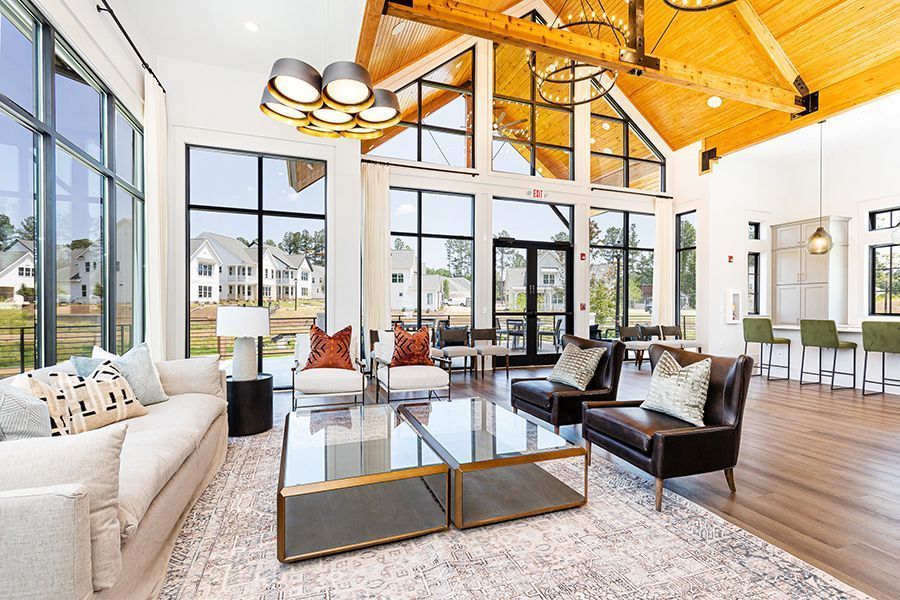 Bright modern living room with vaulted wood ceiling, large windows, white sofa, glass coffee tables, and black chairs