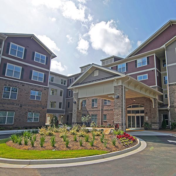 Modern apartment complex entrance with brick buildings, covered entry, and landscaped roundabout under a bright sky