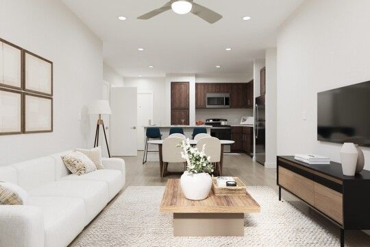 Bright open-concept living room with white sofa, wooden coffee table, and kitchen in the background