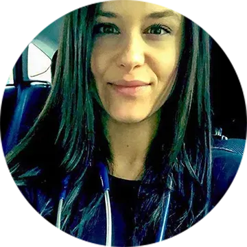 Portrait of a woman with long dark hair, wearing earphones and a dark top, sitting in a car.