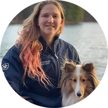 Woman smiling with a collie by the water, wearing a dark jacket outdoors